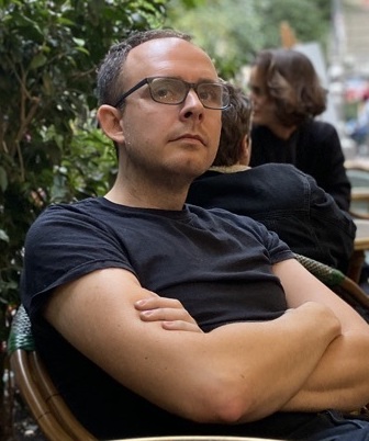 Man sitting in a chair at an outdoor cafe, arms folded