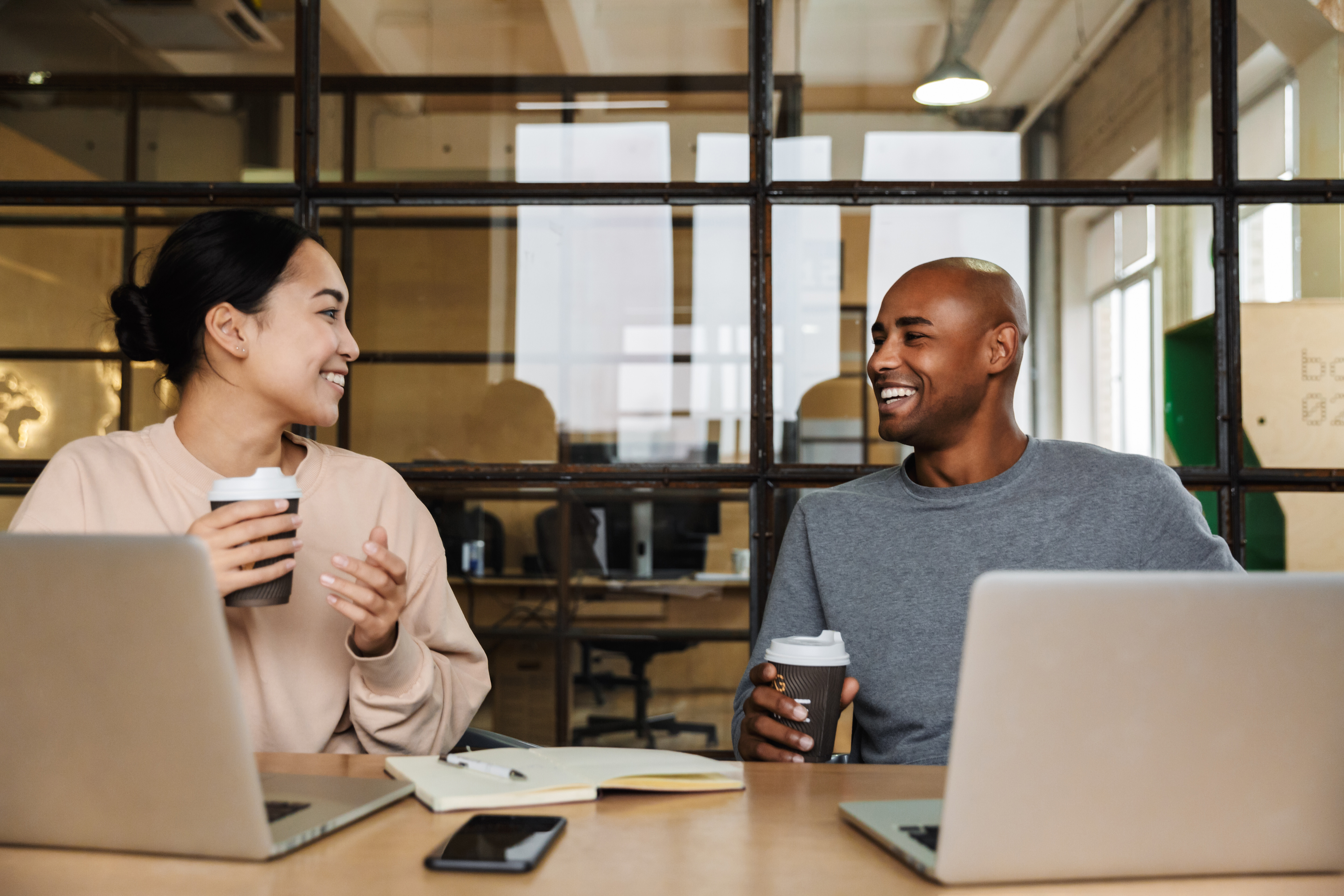 Diverse team of a woman and man smiling while using human-centered security tools on laptops, highlighting the future of SecOps